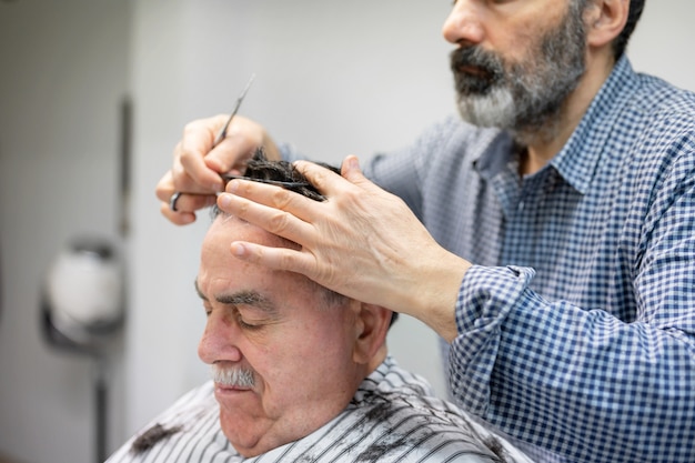 Barber trimming hair of old man at barber shop.