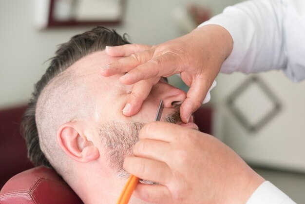 Barber with oldfashioned steel razor shaving bearded man with mohawk