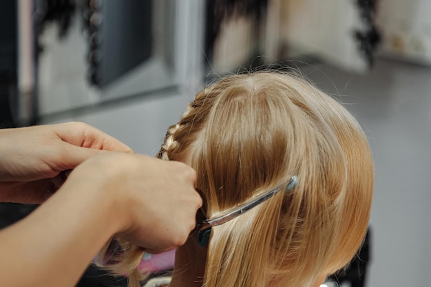 Barber woman make fashionable pretty hairstyle for cute little blond girl