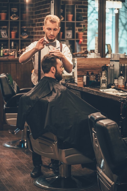 Barber at work. Full length of young bearded man getting haircut by hairdresser 