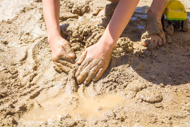 Barefeet kid playing with wet sand. Little boy kneads and models mud on summer sunny day.