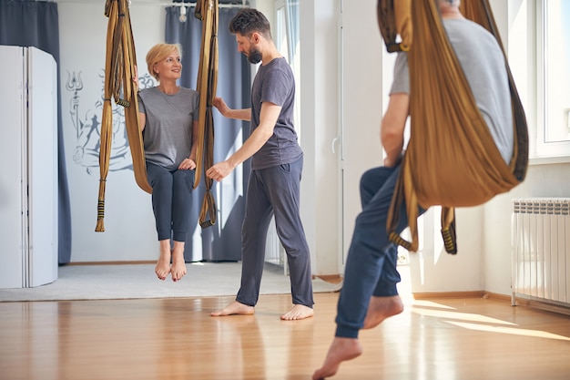 Barefoot blonde Caucasian lady with a short haircut looking at her serious aerial yoga teacher