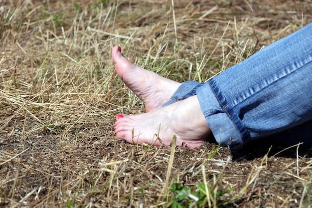 Barefoot female feet in rolled blue jeans resting on dry hay close up view