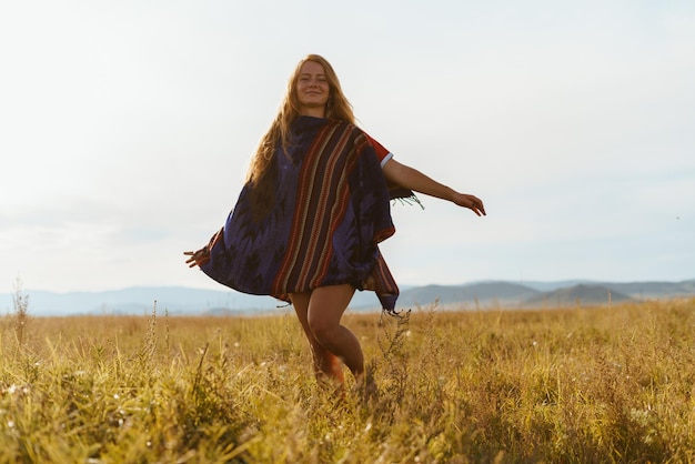 Barefoot girl in striped cape with loose hair running across the field