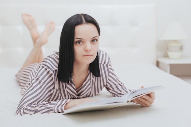 Barefoot young teenage girl looking at the camera lying on her bed reading a book