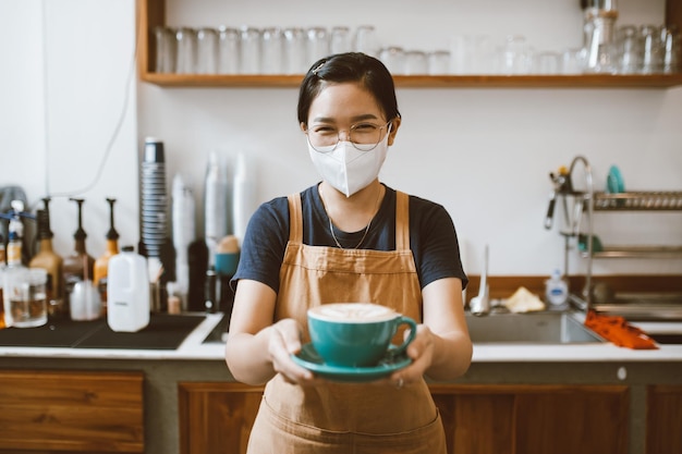 Barista Asian women standing behind the counter and holding coffee cup for offer to customer coffee preparation and service concept small business startup business