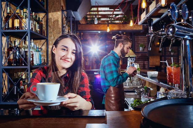 Barista bartender girl holds out cup of coffee in a bar