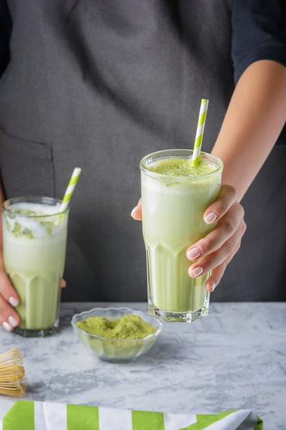 Barista girl holds out green matcha latte tea. Cropped photo. Healthy drink close up