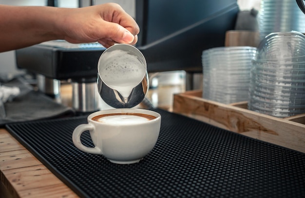 Barista hand pouring milk into coffee making a cappuccino Professional barista preparing coffee