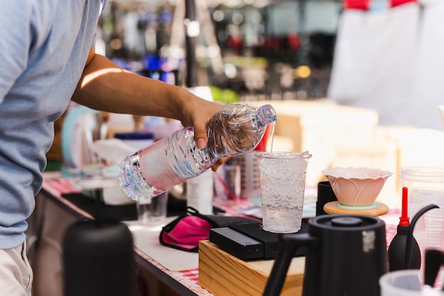 Barista hand pouring water into plastic glass with iced