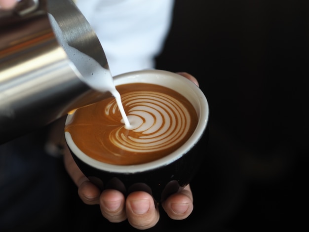 barista hands pouring warm milk for making coffee latte art.