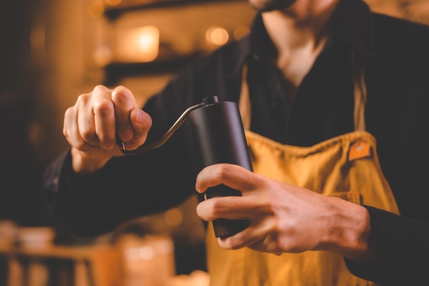 Barista holding hand grinder to making beverage by grinding roasted coffee bean for caffeine drink in kitchen cafe background morning breakfast mill preparation with espresso equipment in brown tone