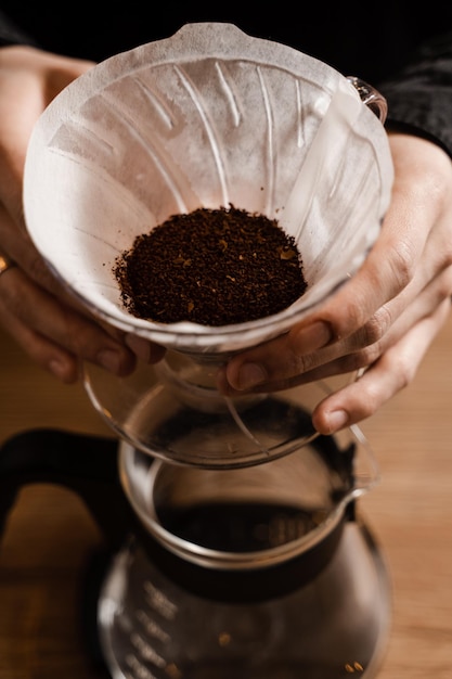 Barista holding pour over device with ground coffee on paper filter before pouring water from drip kettle Process of brewing pour over filter coffee in cafe