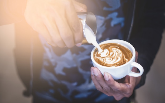 Barista holding and pouring milk for make late art.