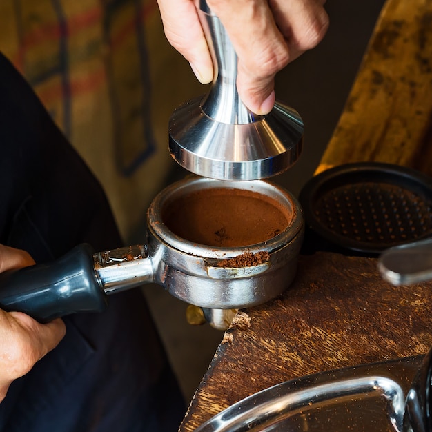 Barista holding tamper and portafilter with coffee for making coffee espresso.