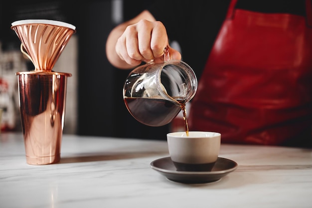 Barista making a drip coffee pouring hot water from kettle over a coffee