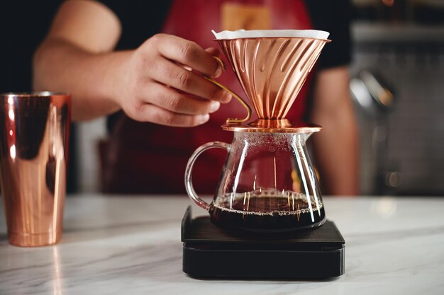 Barista making a drip coffee pouring hot water from kettle over a coffee