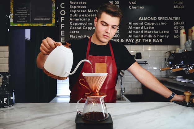 Barista making a drip coffee pouring hot water from kettle over a coffee