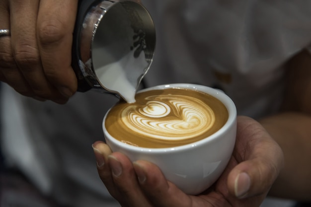 Barista pouring latte froth to make a coffee latte art into the white coffee cup