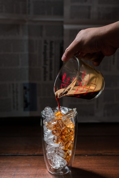 Barista pouring milk into a glass of iced coffee