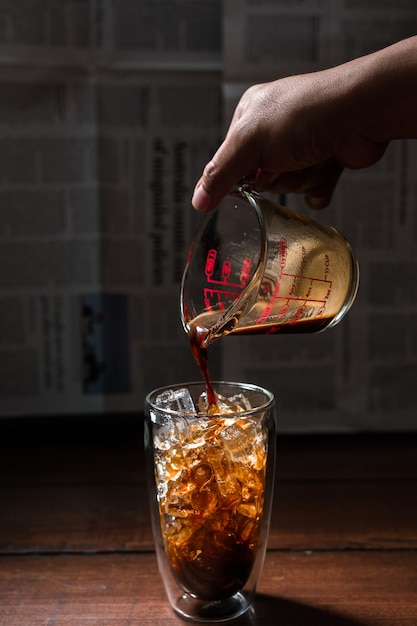 Barista pouring milk into a glass of iced coffee