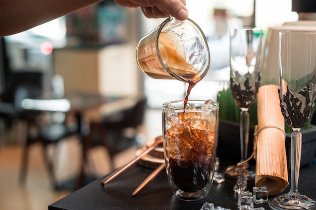 Barista pouring milk into a glass of iced coffee