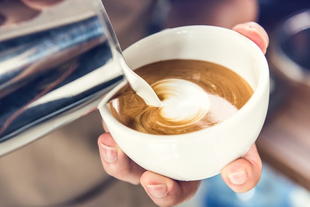 Barista pouring steamed milk into coffee cup making latte art