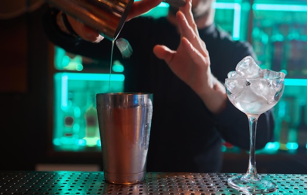 Barman in shirt and apron making an alcoholic drink with ice in a cocktail glass