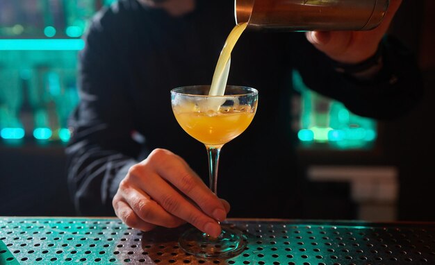 Barman in shirt and apron making an alcoholic drink with ice in a cocktail glass