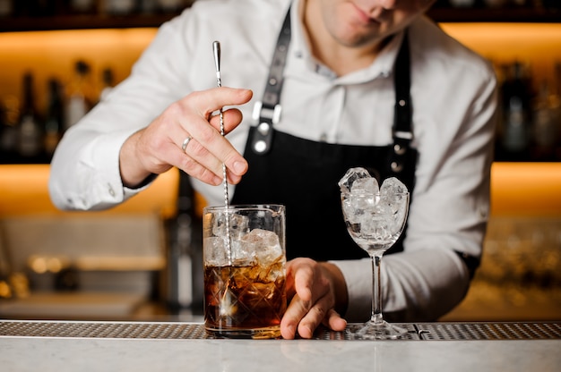 Barman stirring ice cubes with alcoholic drink