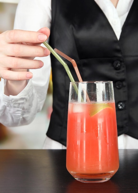 Barmen hand putting cocktail straw into glass on bright background