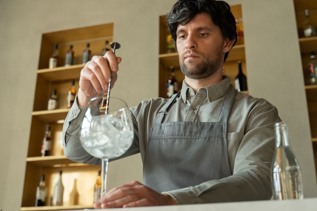 Bartender in the apron stirring an ice cubes in the cocktail glass