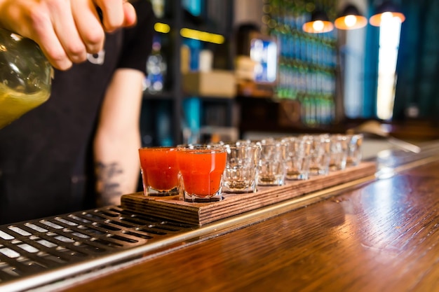 The bartender at the bar pours red tincture into shots Horizontal photo