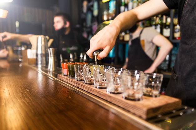 The bartender at the bar pours red tincture into shots Horizontal photo