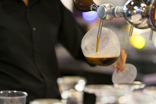 Bartender hands pouring a black beer in a glass.