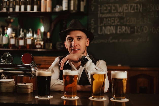 Bartender in hat with a beard at bar counter with beer in glasses