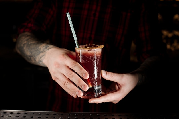 Bartender holding a Sippy Cup cocktail in the glass with a dried orange on the bar counter