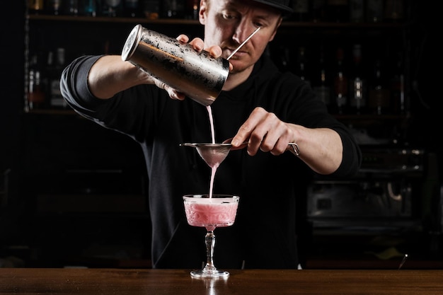 Bartender is pouring pink Clover club alcoholic cocktail in the glass Bartender mixes egg white lemon dry vermouth and gin to prepare the Clover club cocktail