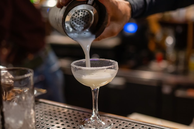 The bartender makes a cocktail at the bar pours a glass of the shaker