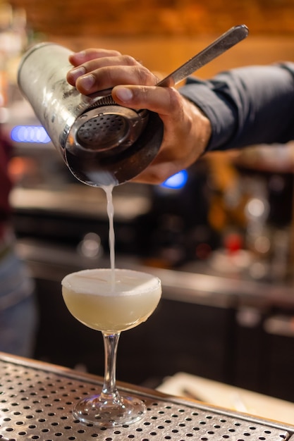 The bartender makes a cocktail at the bar pours a glass of the shaker