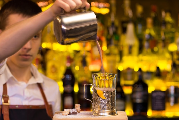 The bartender making cocktail in a nightclub bar. Pouring cocktail into glass..