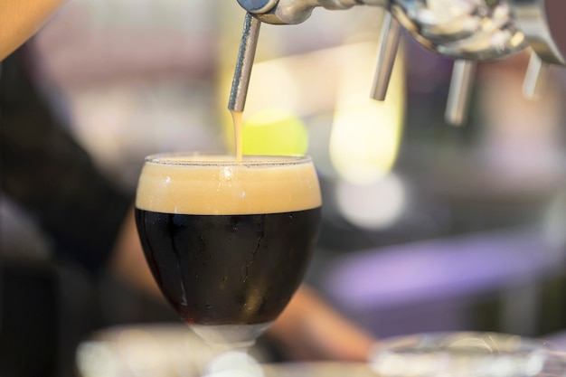 Bartender pouring a black beer in a glass.