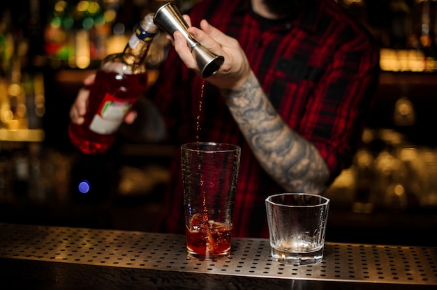 Bartender pouring drink making a Foreign Legion cocktail from the steel jigger to the glass measuring cup on the bar counter