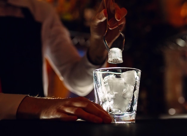 The bartender pours ice into cocktail glasses.