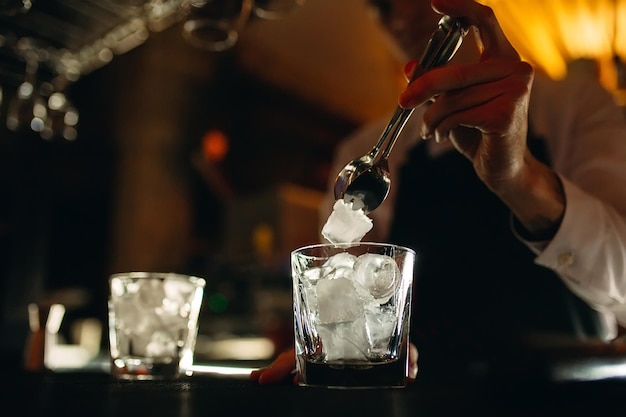 The bartender pours ice into cocktail glasses.