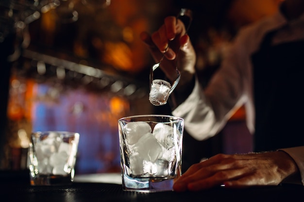 The bartender pours ice into cocktail glasses