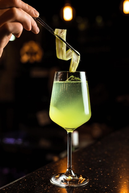 Bartender prepairing a cocktail, adding celery garnish into a wine glass with an iced green color drink