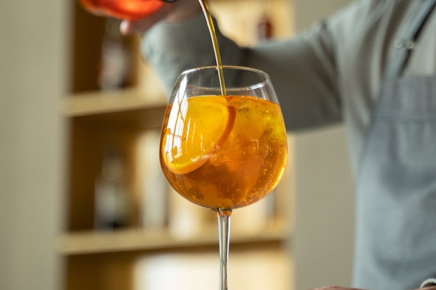 The bartender prepares a cocktail pours orange syrup into a glass