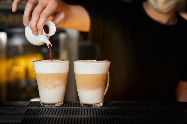 Bartender prepares coffee latte by pouring Black coffee into a glass mug with frothed milk