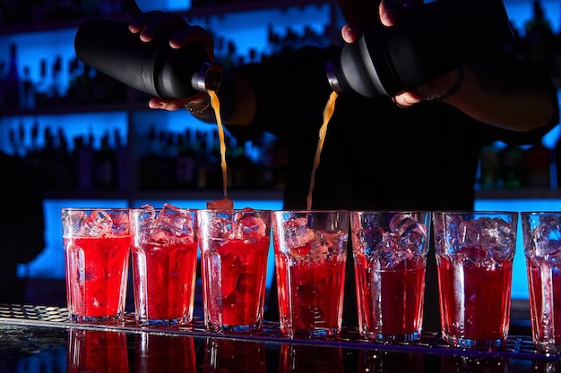 The bartender prepares red cocktails on the bar counter using shakers